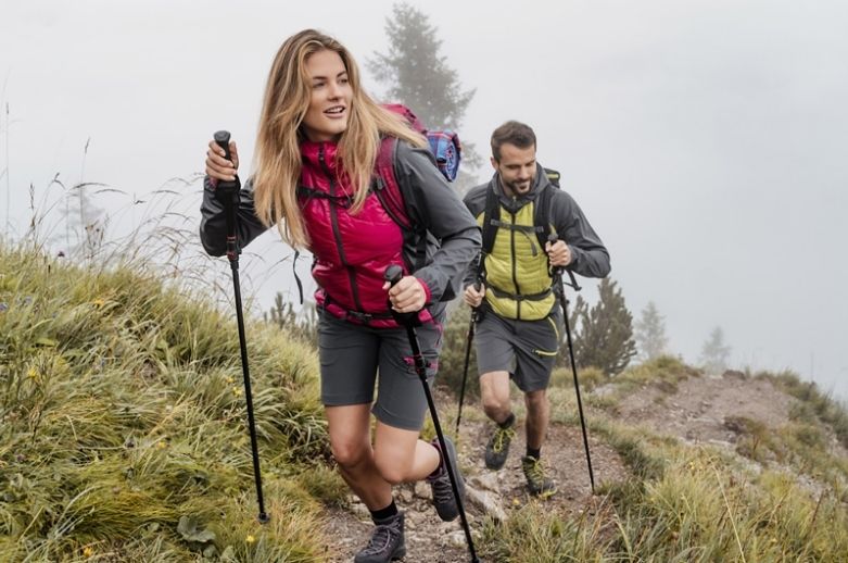 Persona caminando con bastones de trekking en un sendero de montaña, mostrando técnica correcta y postura adecuada.